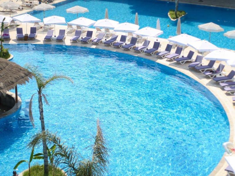 Rundes Außenpool mit Sonnenliegen und Sonnenschirmen vor einem Hotelgebäude