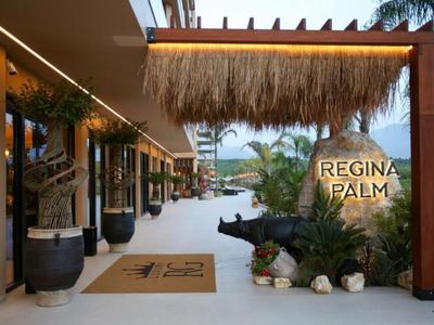 Hotel entrance area with palm trees, plants, and a sign reading 'Regina Palm'.
