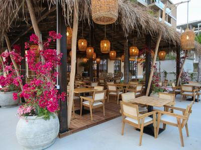 Offener Pavillon mit Holztischen und Stühlen, umgeben von Pflanzen und Laternen in einem Hotelbereich.