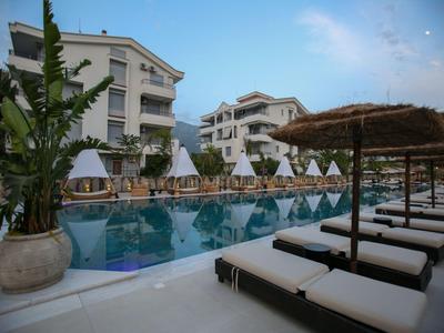 Moderner Poolbereich mit Liegen, Schirmen und weißen Gebäuden im Hintergrund bei klarem Himmel.