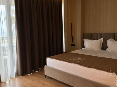 Nowoczesny pokój hotelowy z dużym łóżkiem, brązowymi zasłonami, drewnianą podłogą i delikatnym oświetleniem.