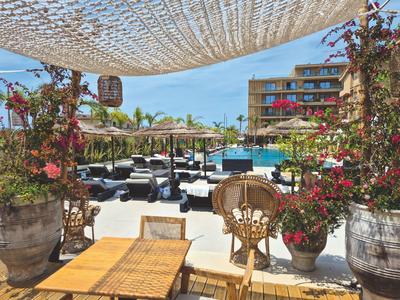 Sonnenterrasse mit Pool, loungemöbeln und großen Blumentöpfen in einem Hotelresort.