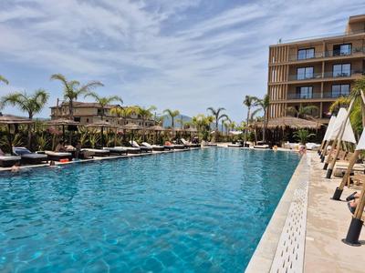 Großer Außenpool mit Liegestühlen und Palmen in einem Hotelresort bei klarem Himmel.