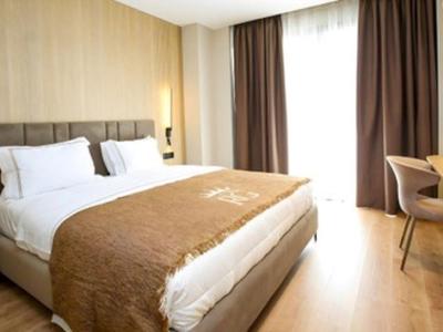 Bright hotel room with double bed, wooden floor, and large window with curtains.
