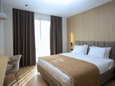 Modernes Hotelzimmer mit großem Bett, braunen Vorhängen und Holzvertäfelung an der Wand.