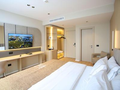 Modernes Hotelzimmer mit großem Bett, Flachbildfernseher und heller, neutraler Einrichtung.