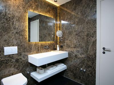 Modernes Badezimmer mit beleuchtetem Spiegel, weißem Waschbecken und braun gemusterten Wänden.