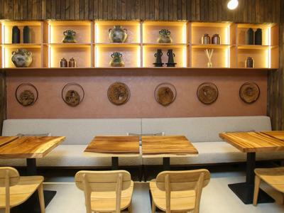 Gemütlicher Essbereich mit Holztischen, Stühlen und Wandregal mit dekorativen Vasen und Tellern.