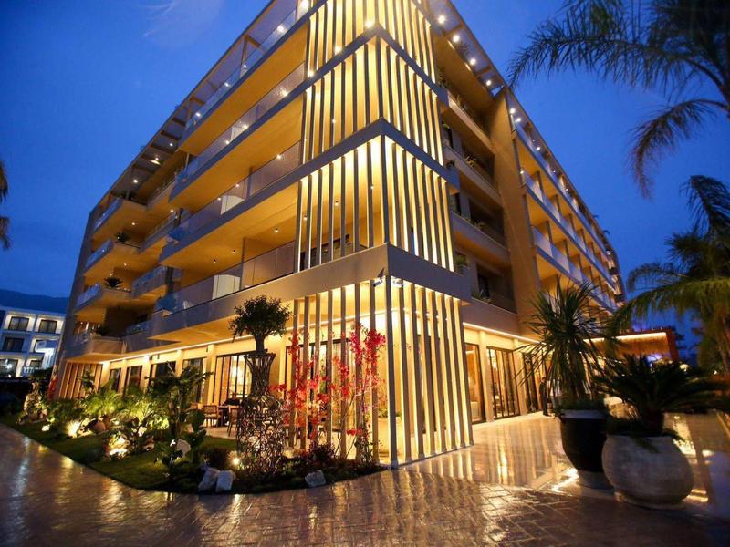 Modernes Hotelgebäude mit beleuchteten Balkonen und Palmen bei Dämmerung