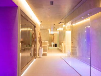 Modern gestalteter Hotelflur mit warmem und violettem Licht und Glaswänden.