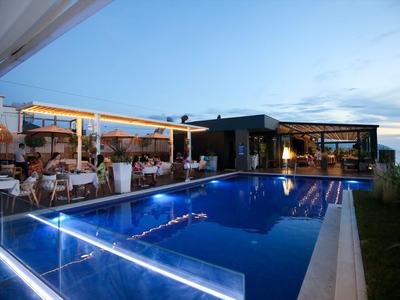 Moderner Außenpool mit beleuchteter Umrandung neben einem Restaurant bei Sonnenuntergang.