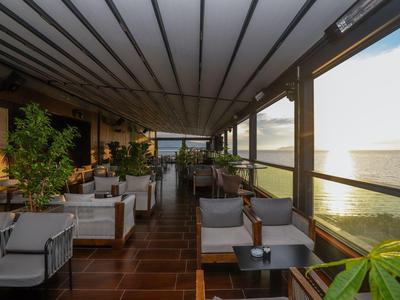 Überdachte Terrasse mit Gartenmöbeln und Blick auf das Meer bei Sonnenuntergang