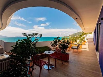 Balkon se židlemi, rostlinami a výhledem na moře za jasné oblohy.