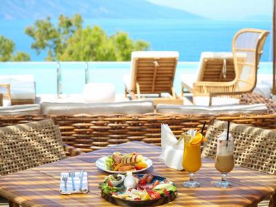 Tisch mit Frühstück und Getränken, Pool und Meer im Hintergrund an einem sonnigen Tag.