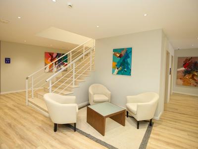 Moderner Aufenthaltsraum mit weißen Sesseln, Glastisch, Treppe und bunten Gemälden an der Wand.