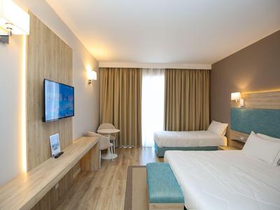 Modernes Hotelzimmer mit zwei Betten, Schreibtisch und Fernseher an der Wand.