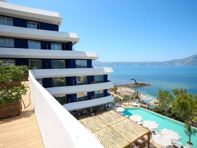Blick von einem Balkon auf ein modernes Hotel, Pool und Meer unter klarem Himmel.