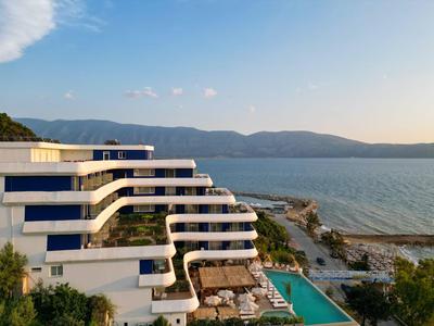 Modernes Hotel mit terrassenförmigen Balkonen, Pool und Blick auf das Meer bei Sonnenuntergang.