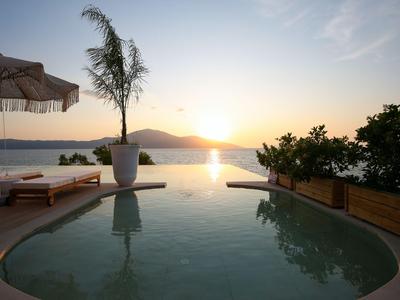 Infinity-Pool mit Palmen und Sonnenliegen bei Sonnenuntergang am Meer