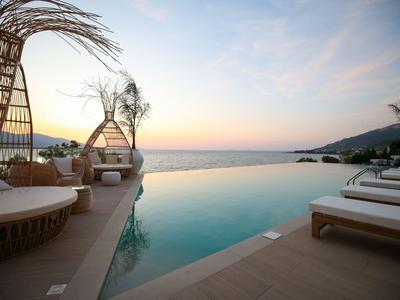 Infinity-Pool mit Liegestühlen und einzigartigen Überdachungen, Blick auf das Meer bei Sonnenuntergang.