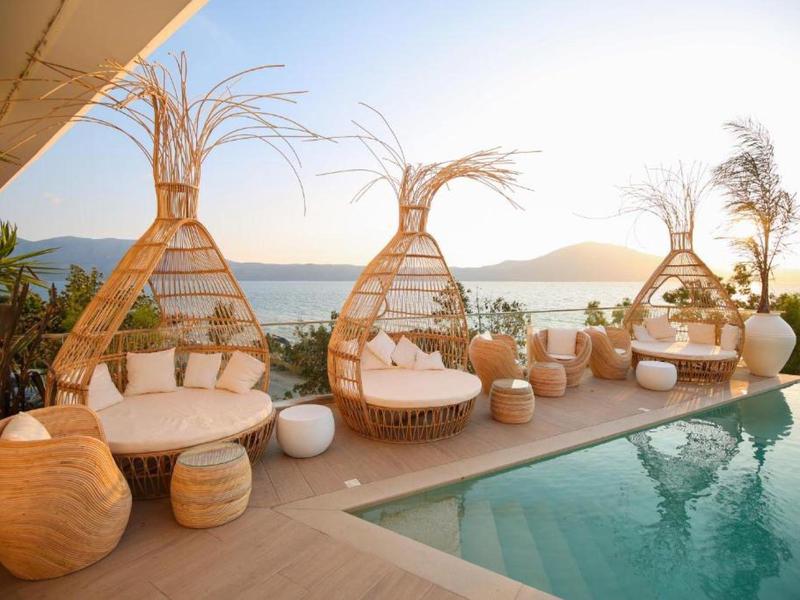 Luxuriöse Strandlounge mit Rattan-Sesseln und Blick auf den Pool und das Meer bei Sonnenuntergang.