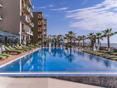 Nowoczesny basen z leżakami i palmami obok hotelu pod słonecznym niebem.