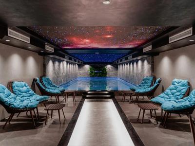 Moderner Innenpoolbereich mit blauen Sitzkissen und stimmungsvoller Beleuchtung unter gedecktem Dach.