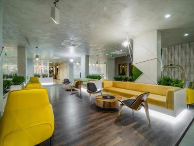 Nowoczesny salon hotelowy z żółtymi sofami, drewnianą podłogą i stylowymi krzesłami.