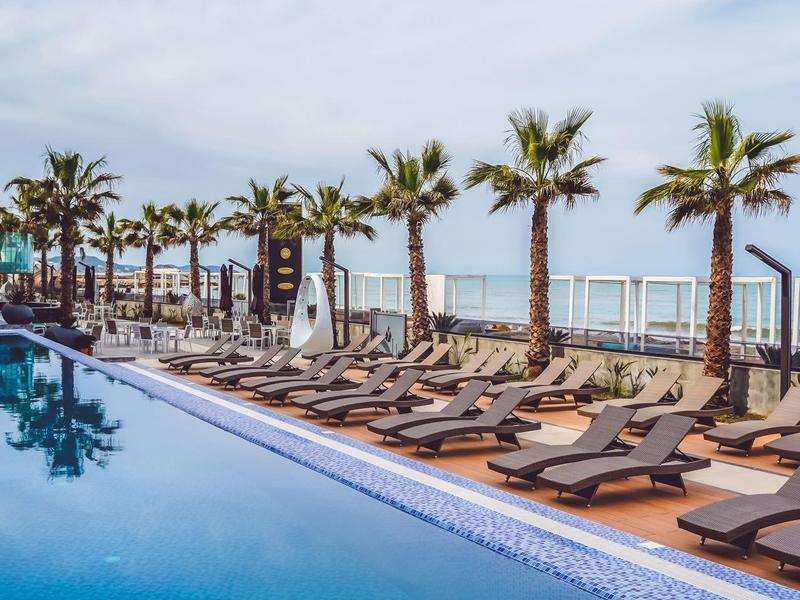 Luxuriöser Poolbereich mit Sonnenliegen und Palmen am Meer.