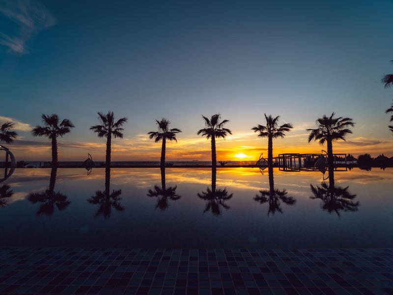 Sonnenuntergang mit Palmen und ihrer Spiegelung in einem ruhigen Pool.