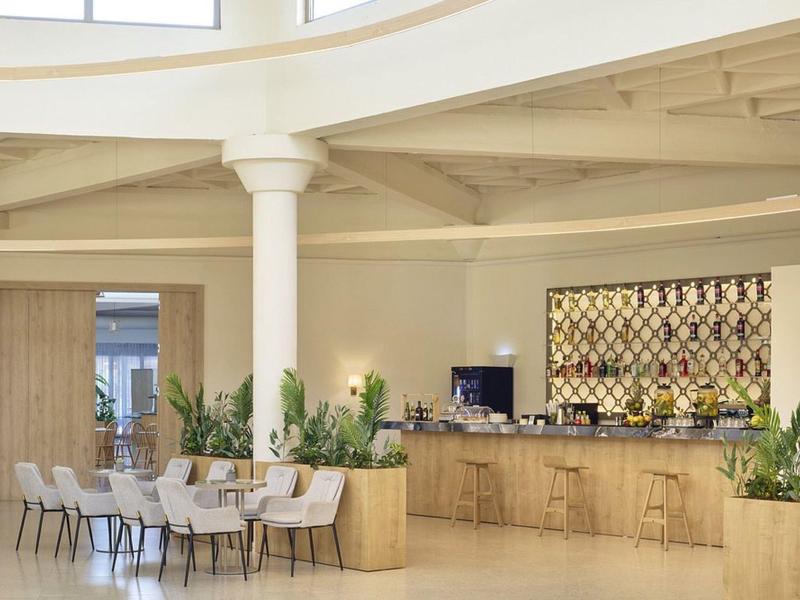 Heller Hotel-Loungebereich mit Tischen, Stühlen, Pflanzen und einer Bar mit Holzfront.