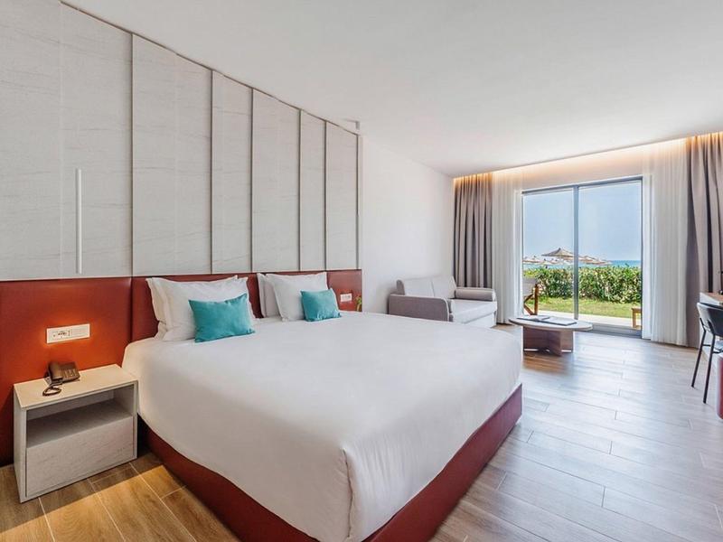 Modernes Hotelzimmer mit großem Bett, Sitzbereich und Blick auf den Garten.