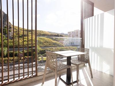 Balcon avec table et deux chaises donnant sur des collines verdoyantes et des bâtiments au soleil.