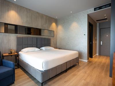 Chambre d'hôtel moderne avec lit double, sol en bois et un fauteuil bleu à côté du lit.