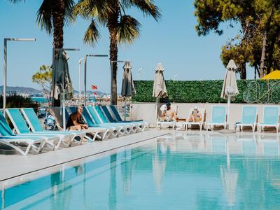 Une piscine claire avec des transats blancs et des palmiers en arrière-plan par une journée ensoleillée.
