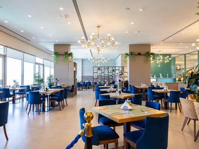 Restaurant lumineux et moderne avec des chaises bleues, des tables en bois et de grandes fenêtres laissant entrer la lumière du jour.