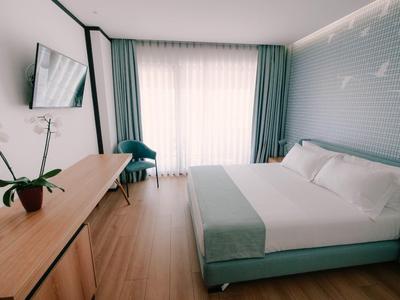 Helles Schlafzimmer mit großem Bett, Holzfußboden, grün-blauen Vorhängen und TV an der Wand.