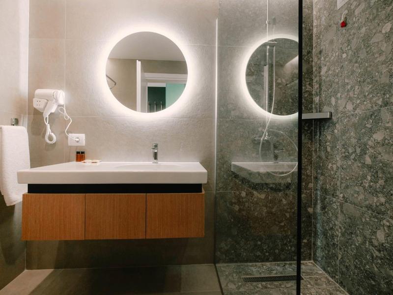 Modernes Badezimmer mit beleuchtetem runden Spiegel, hölzernem Waschbeckenunterschrank und Glasdusche.