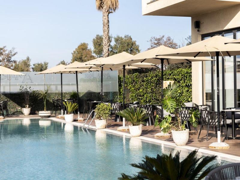 Moderner Außenpool mit weißen Sonnenschirmen, Pflanzen in Töpfen und Sitzbereichen neben einem Gebäude.