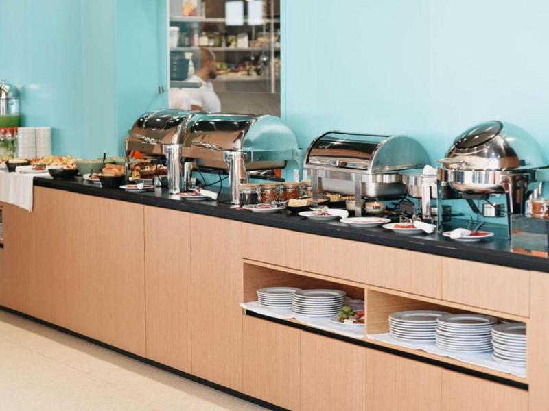 Buffet mit warmen Speisen in Edelstahlbehältern auf schwarzer Theke vor hellblauen Wand.