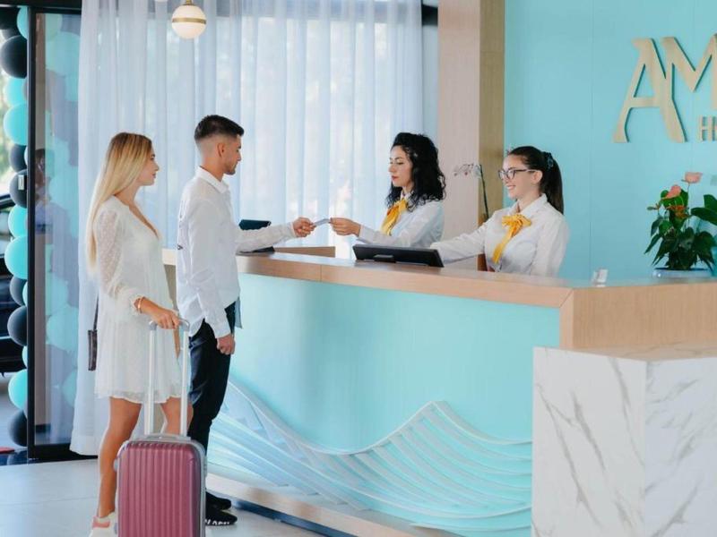 Ein Paar checkt im hellen Hotel mit türkisfarbener Rezeption und freundlichen Empfangsmitarbeitern ein.