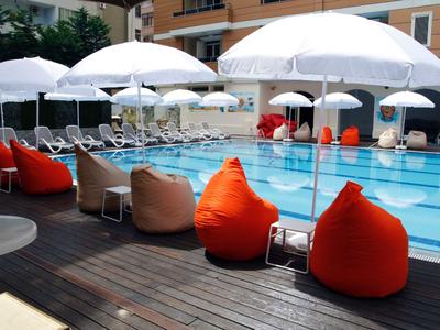 Moderní bazénová zóna s bílými slunečníky a barevnými sedacími vaky vedle hotelu.