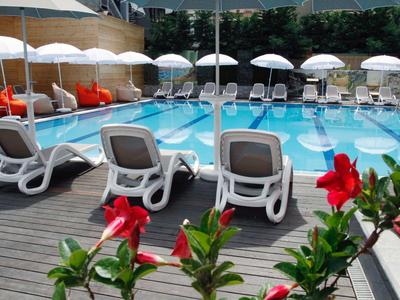 Bazén se lehátky, slunečníky a červenými květy v popředí.