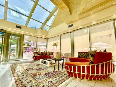 Pohodlná hotelová hala s velkými okny, kobercem a červenými křesly.