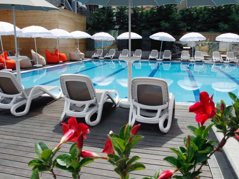 Schwimmbecken mit Liegestühlen und weißen Sonnenschirmen, rote Blumen im Vordergrund.
