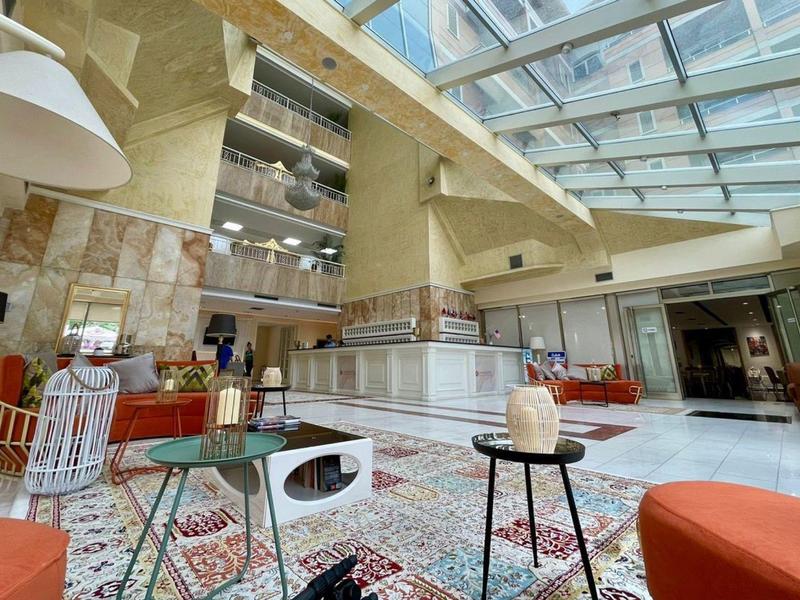 Helle Lounge mit Glasdach, gemütlichen Sitzgelegenheiten, Teppichen und modernen Möbeln.