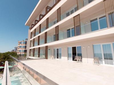 Moderner Balkon mit Glasgeländer und weißen Fliesen, hell und offen bei klarem Himmel.