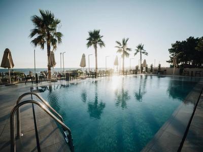 Pool mit klarem Wasser, Palmen und Sonnenschirmen am Strand bei Sonnenuntergang.