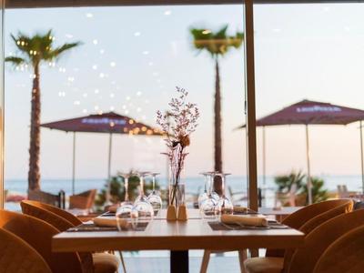Table élégante avec des verres devant de grandes fenêtres donnant sur des palmiers et des parasols de plage.