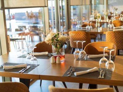 Restaurant moderne avec chaises en bois, tables dressées et compositions florales à l'intérieur.